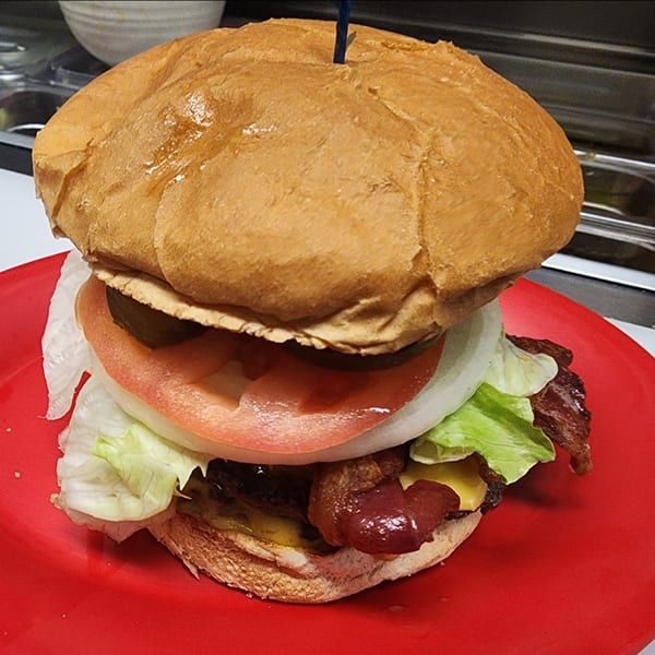 A large St Clair Coney Island burger with bacon, cheese, lettuce, tomato, onion, and pickles on a red plate.