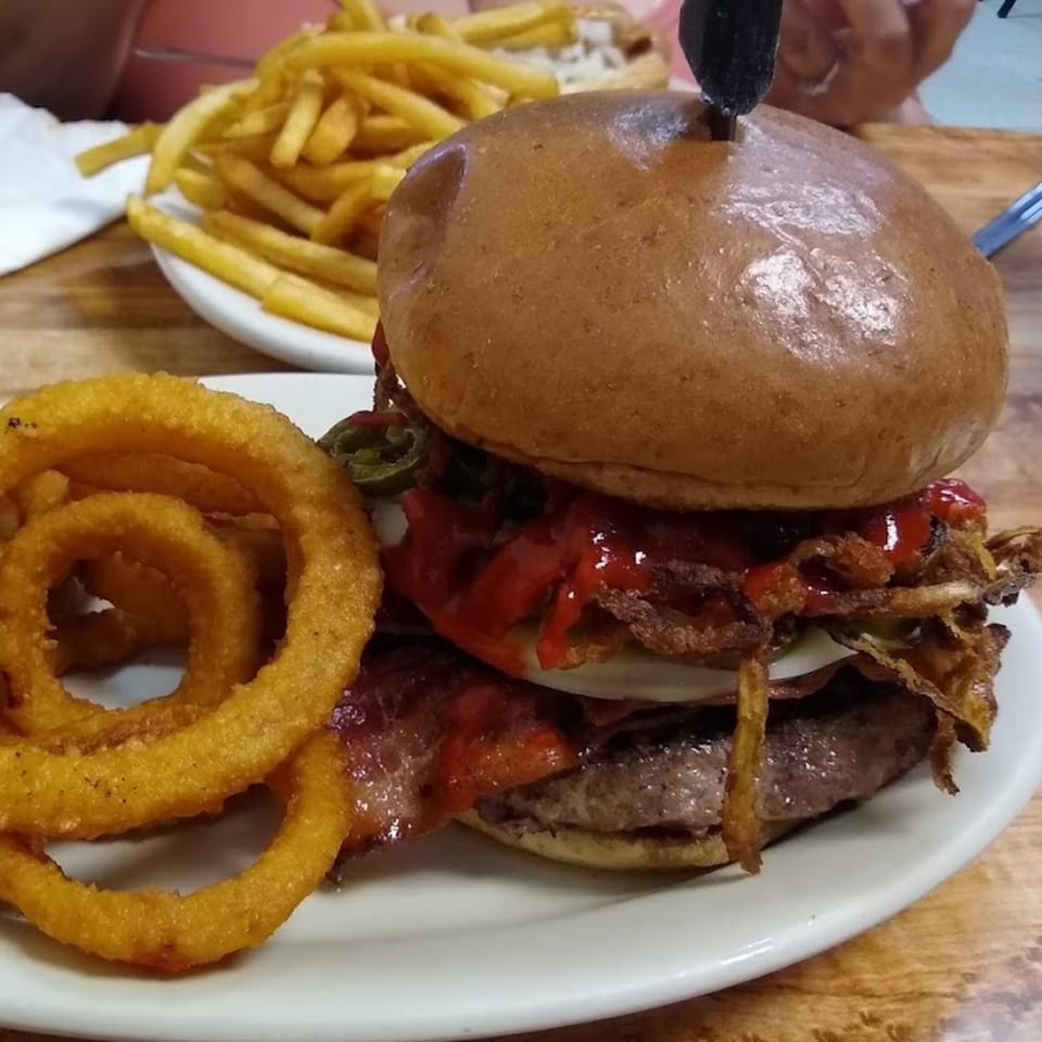 A St Clair Coney Island burger with bacon, onion rings, and fries on a white plate.