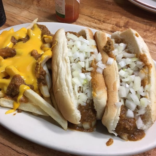 Two chili dogs with diced onions and a side of chili cheese fries on a white plate.