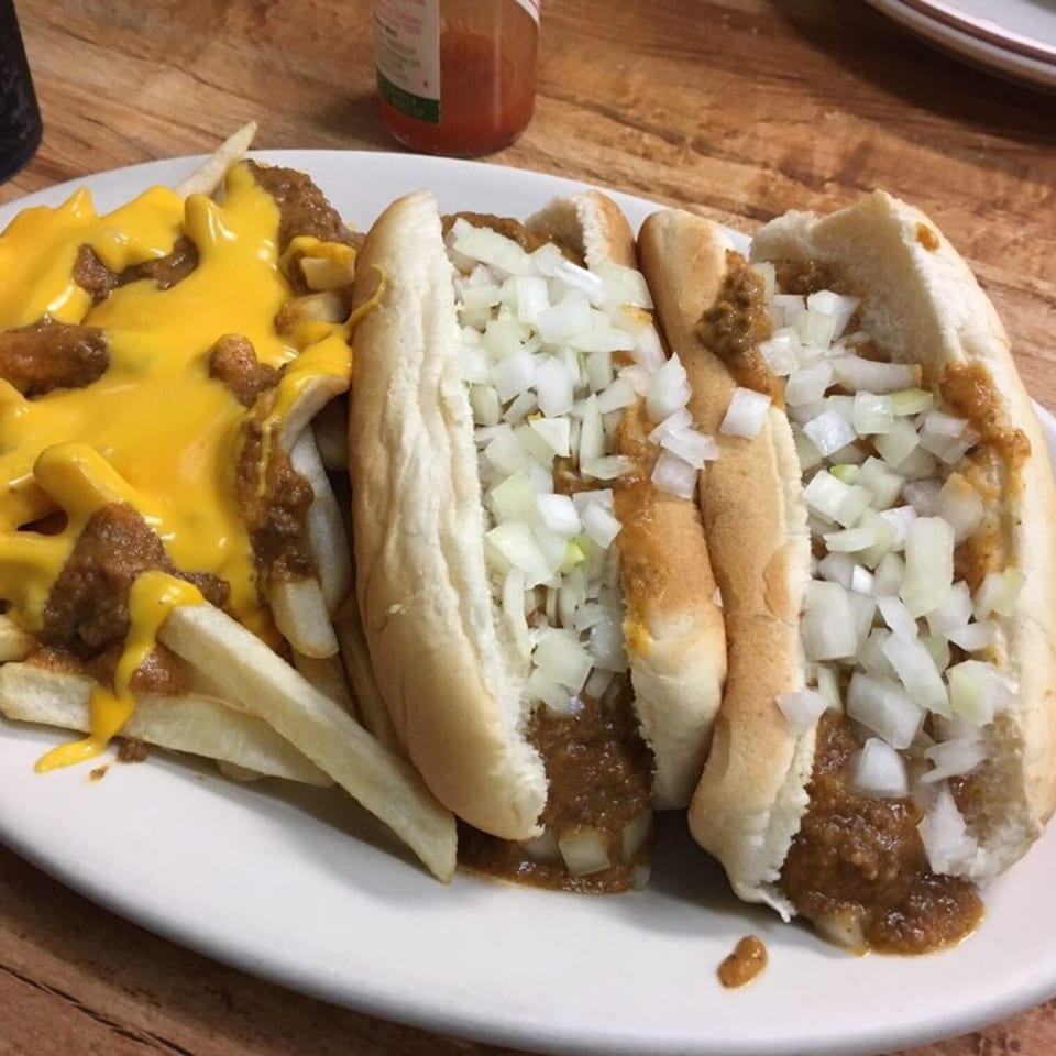 Two chili dogs with diced onions and a side of chili cheese fries on a white plate.