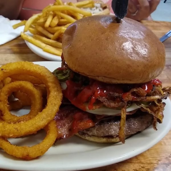 A St Clair Coney Island burger with bacon, jalapeños, and onion rings, with fries in the background.